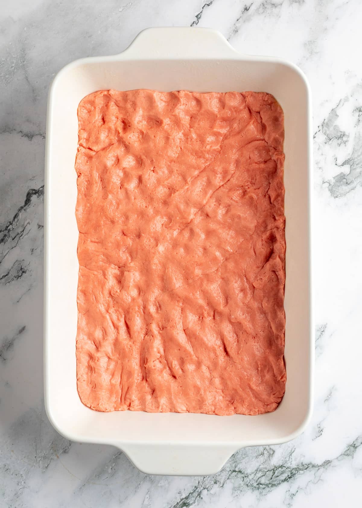 strawberry chess bar dough pressed into a white baking dish on a white marble board