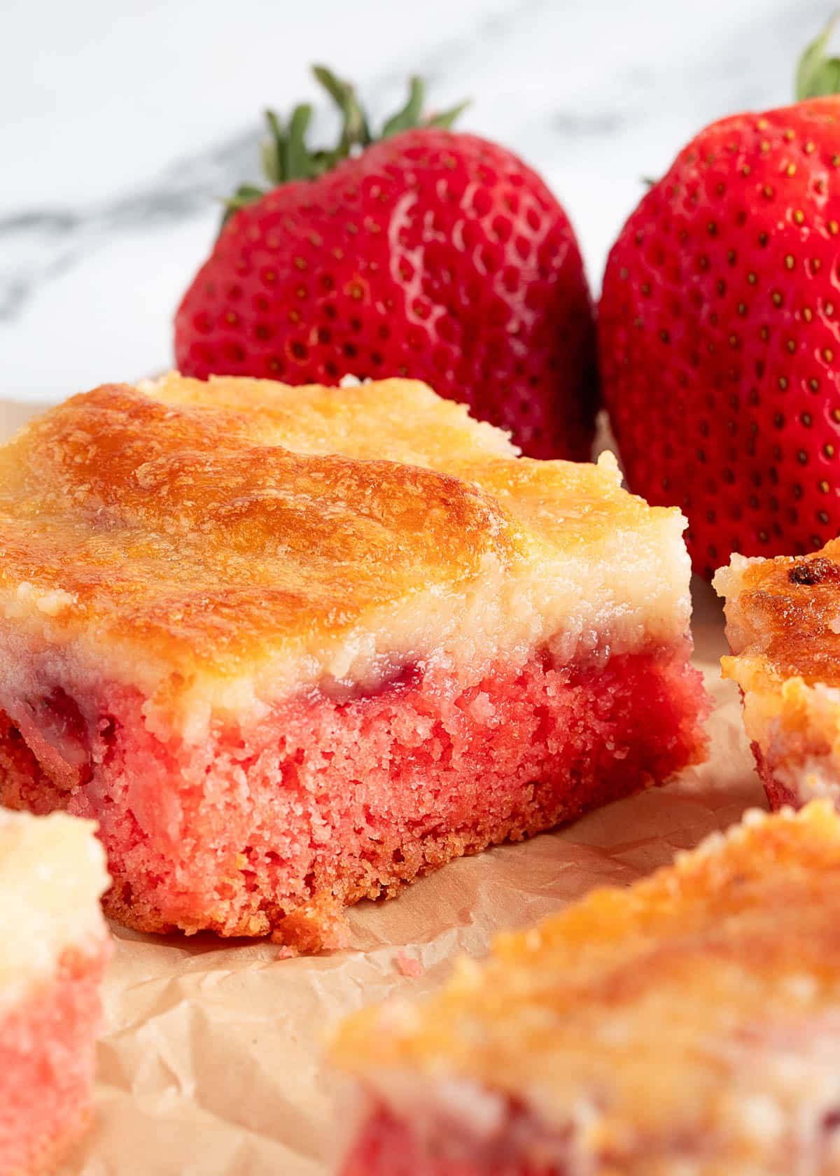 closeup of a strawberry chess square on parchment paper next to whole strawberries