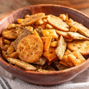Close-up of Dill Ranch Snack Mix served in a wooden bowl, featuring a variety of seasoned crackers including butter, wheat, cheese, and oyster crackers coated in visible herbs and spices.