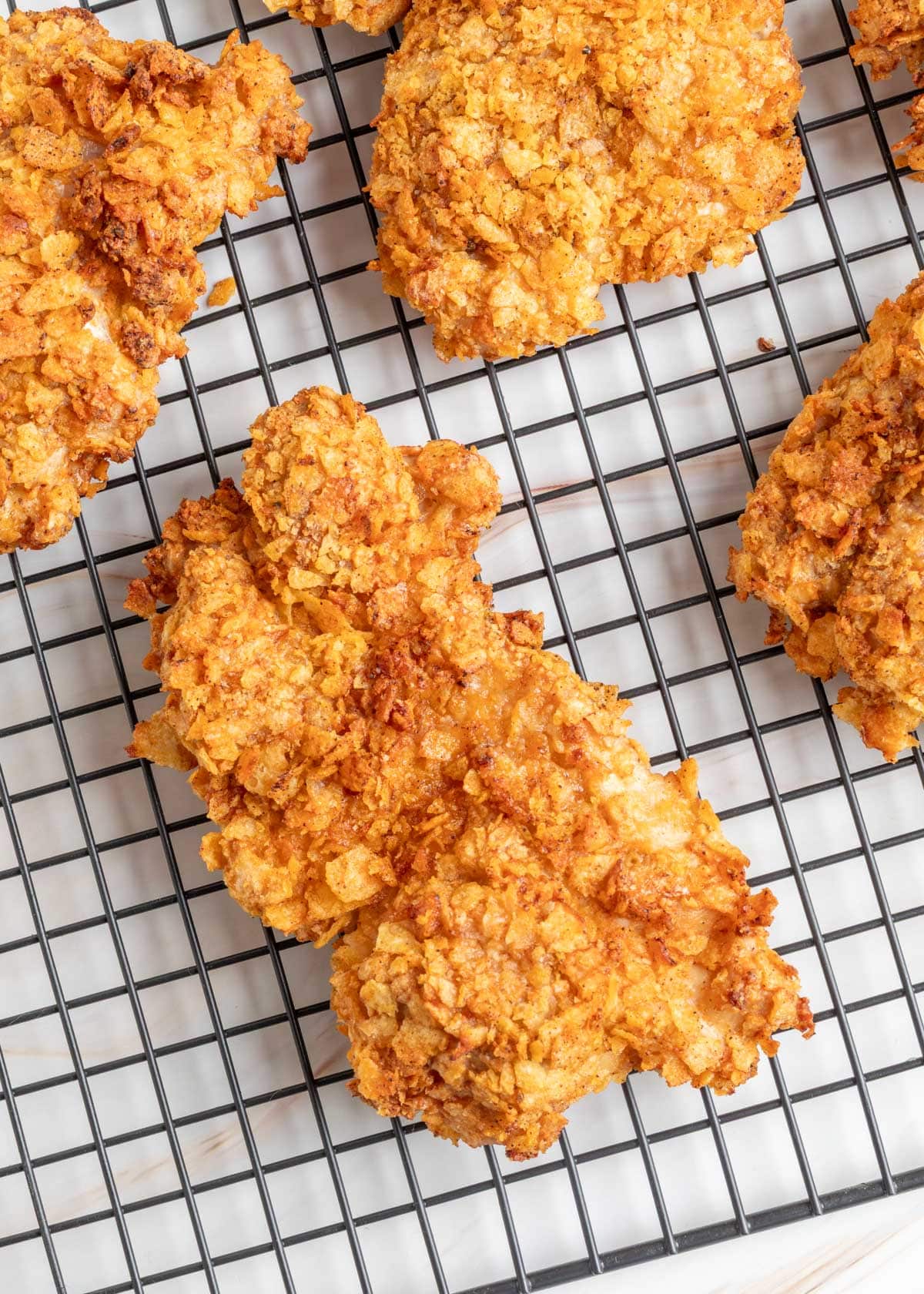 Golden brown potato chip&ndash;crusted chicken thighs cooling on a wire rack after air frying. The crust is visibly crisp with uneven, craggy texture from crushed chips.