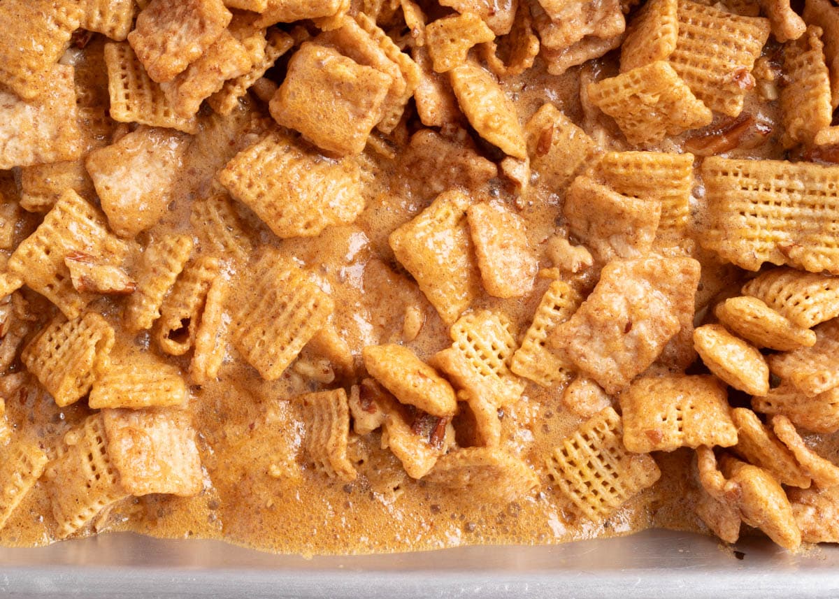 Close-up shot of the cereal mixture coated in bubbling cinnamon praline glaze during the baking process, showing the texture of the sticky, caramel-like coating.