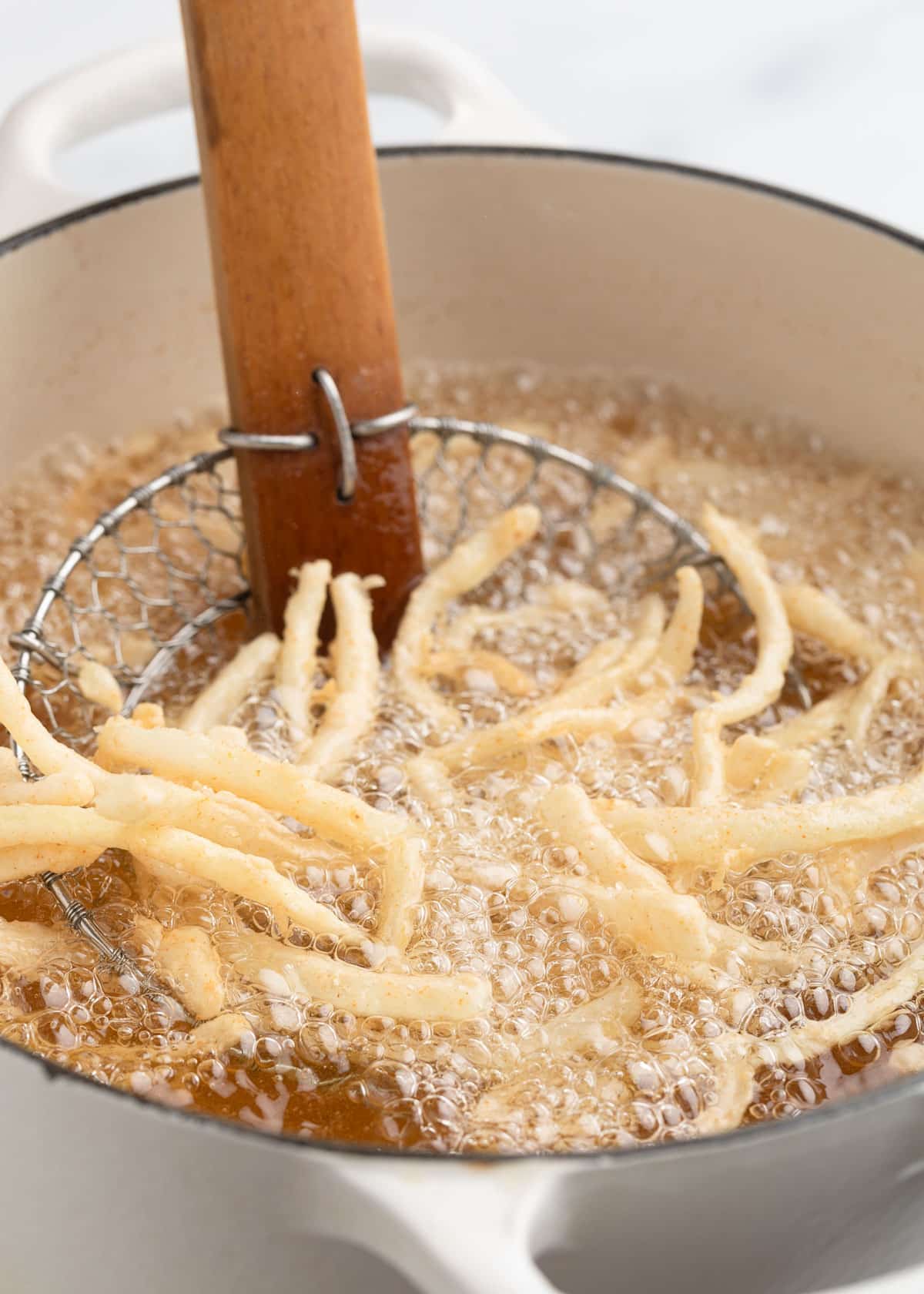 Breaded onions actively frying in hot oil, bubbling vigorously in a Dutch oven as they begin to crisp.