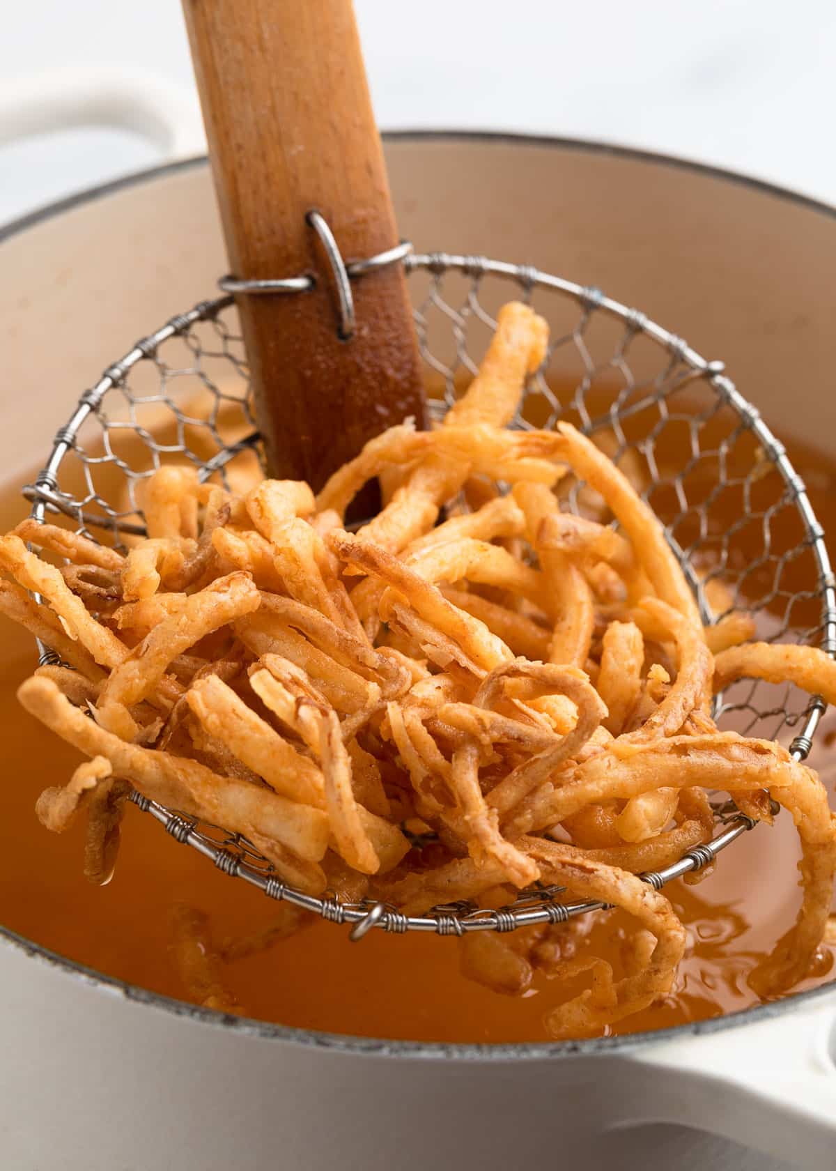Golden brown French fried onions resting in a wire spider skimmer over a pot of oil, just lifted from frying.