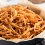 A close-up of a black bowl lined with parchment paper, filled with crispy homemade French fried onions