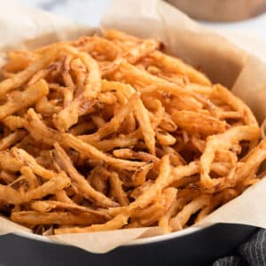 A close-up of a black bowl lined with parchment paper, filled with crispy homemade French fried onions