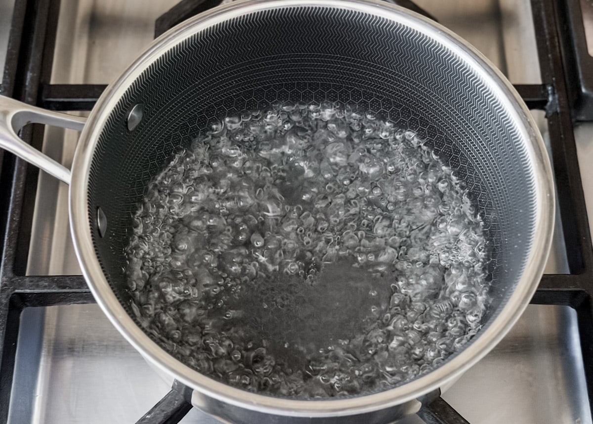 A close-up of a saucepan on a stovetop with sugar water at a rolling boil, ready for the next step in the recipe.