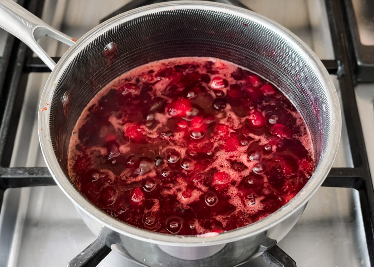 Cranberries simmering and breaking down in the saucepan as the sauce thickens and deepens in color.