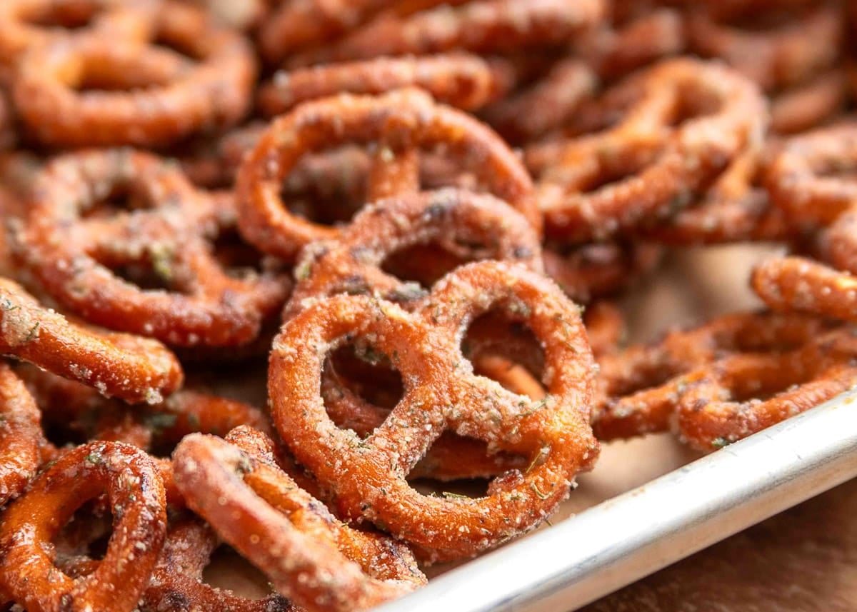 Macro shot of ranch-seasoned mini pretzels on a baking sheet, highlighting the texture of the dry seasoning coating with visible herbs and spices clinging to each pretzel.