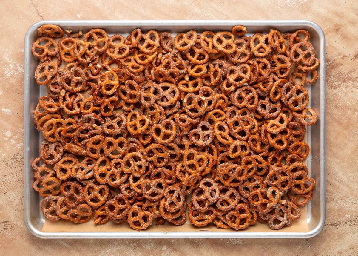 Closeup of a metal baking sheet filled with seasoned Ranch Pretzels arranged in an even layer before baking, set on a light tan surface.