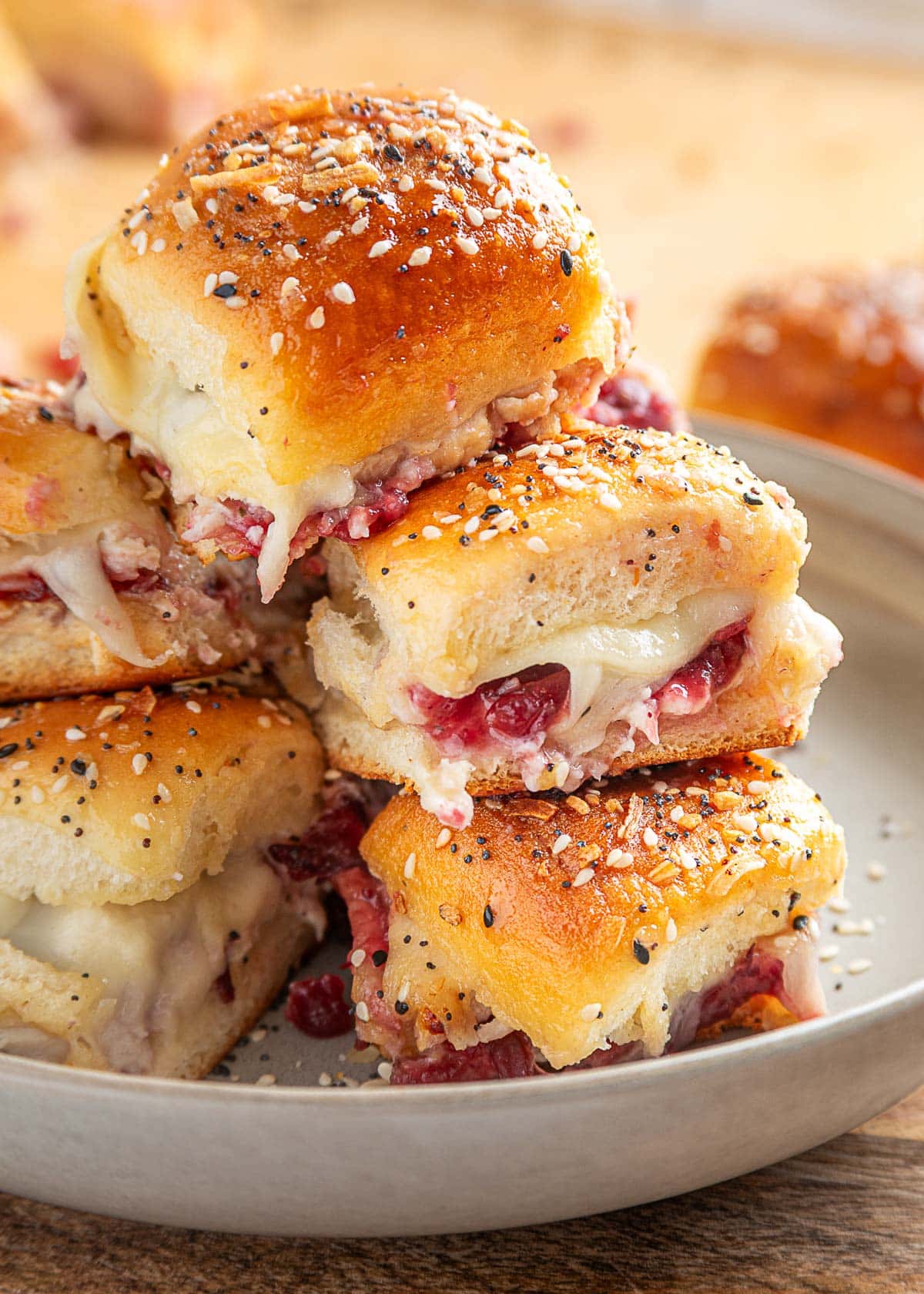 Stack of baked turkey cranberry sliders on a plate, made with golden Hawaiian rolls, cranberry sauce, melted cheese, and a sprinkle of everything bagel seasoning on top.