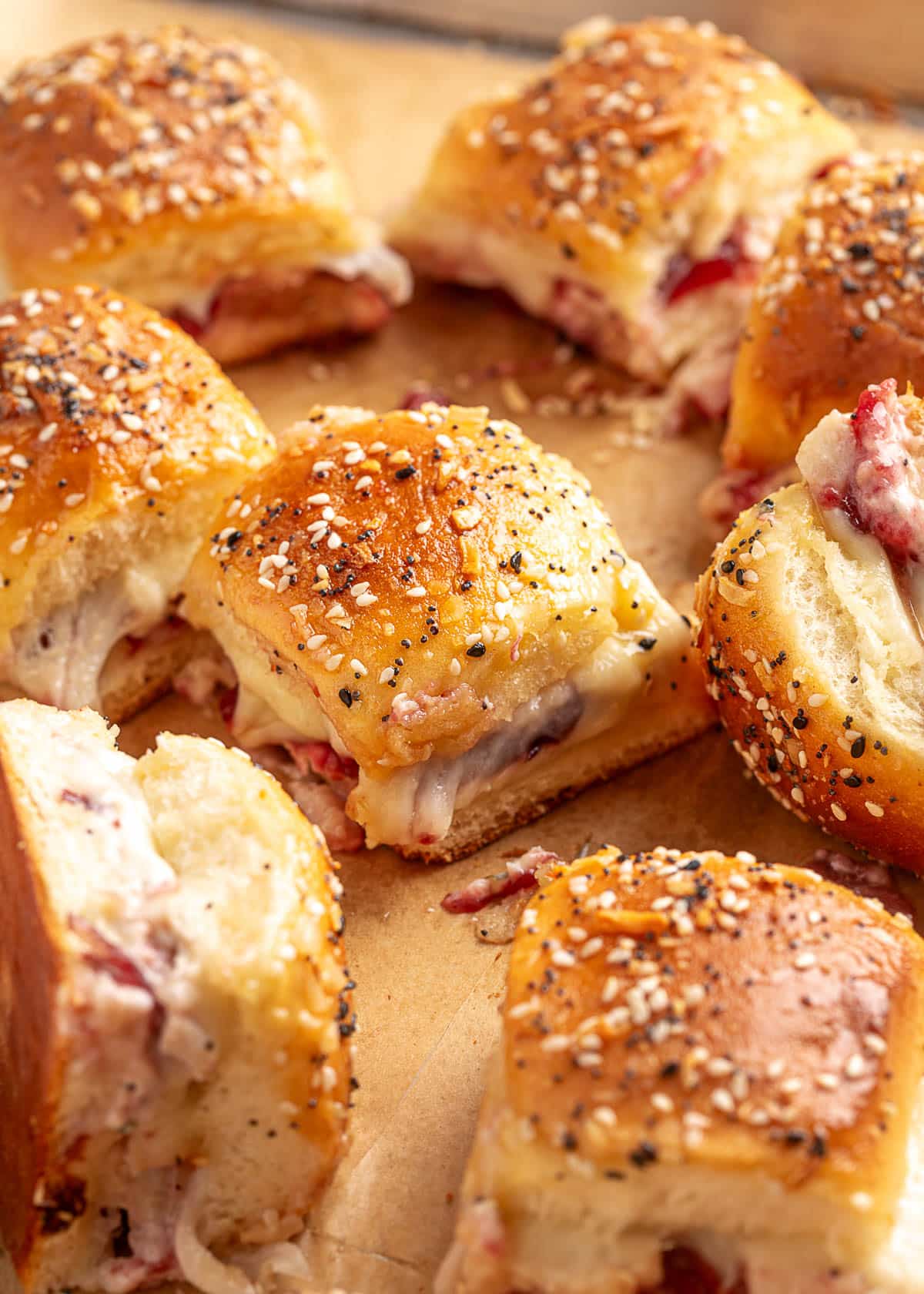 Freshly baked turkey cranberry sliders on everything-seasoned rolls, cut and separated on a parchment-lined baking sheet. Melty provolone, cranberry sauce, and sliced turkey are visible between the golden buns.