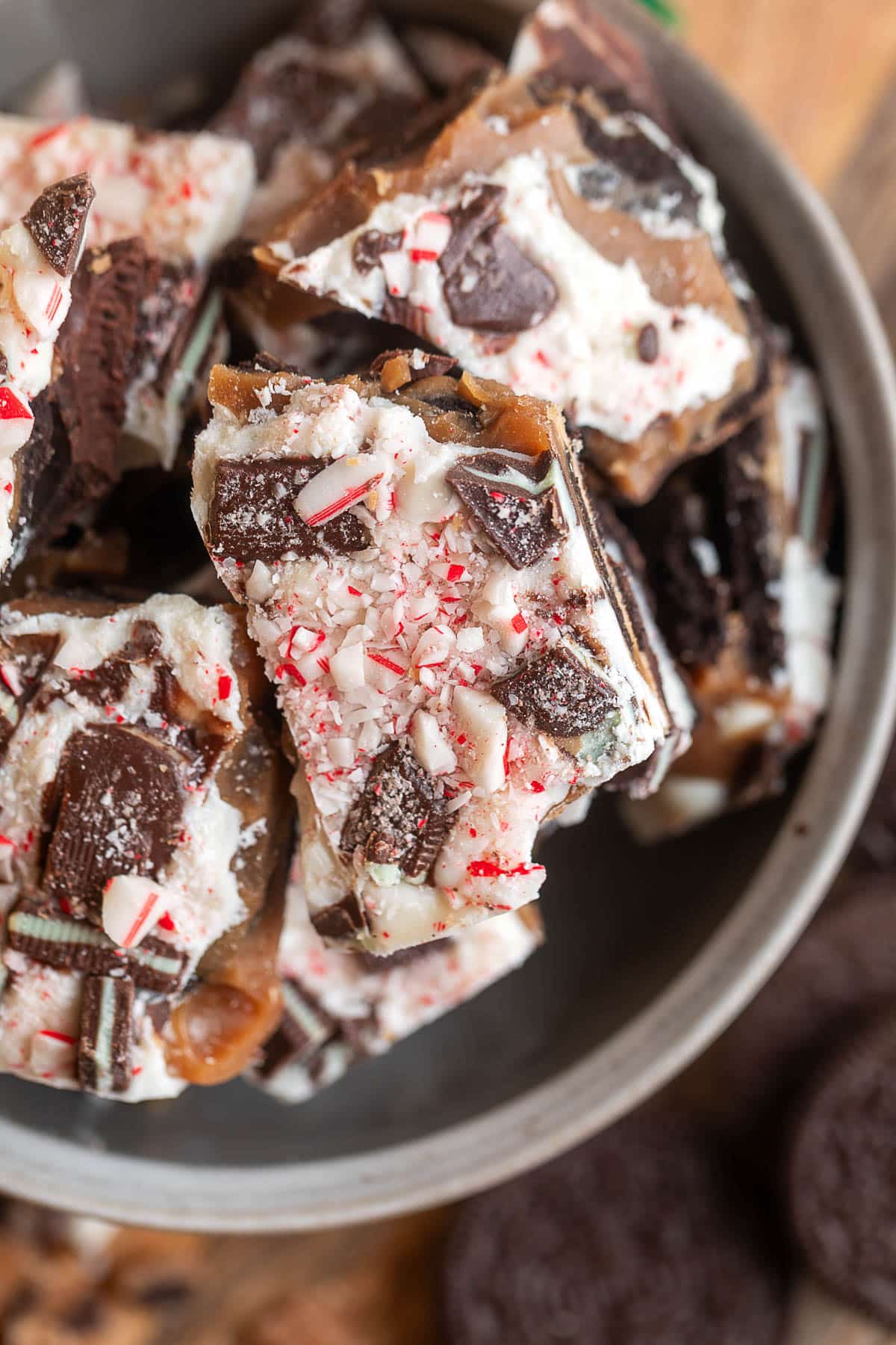 Close-up of broken pieces of Oreo mint toffee bark in a bowl, showing layers of toffee, white chocolate, chopped Andes mints, and crushed peppermint candy.