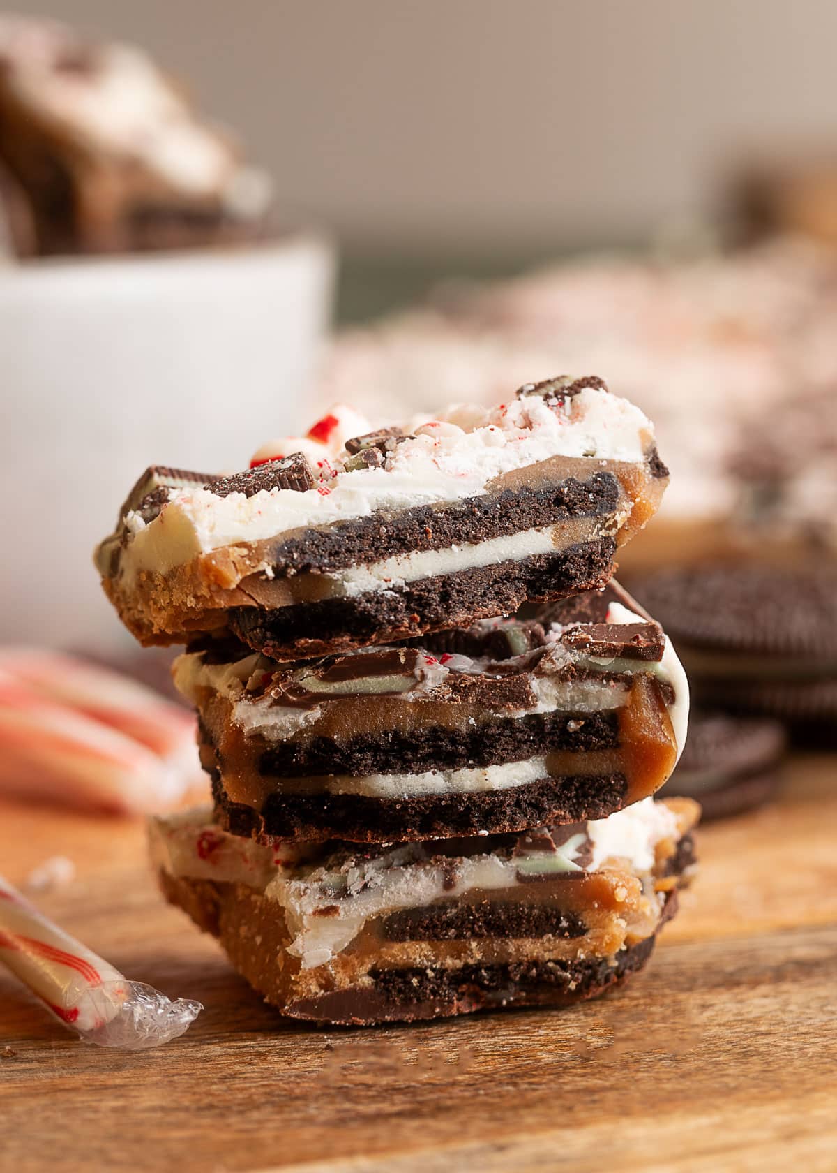 Stack of Oreo mint toffee bark pieces on a wooden surface, showing defined layers of chocolate cookies, toffee, white chocolate, Andes mints, and crushed peppermint.