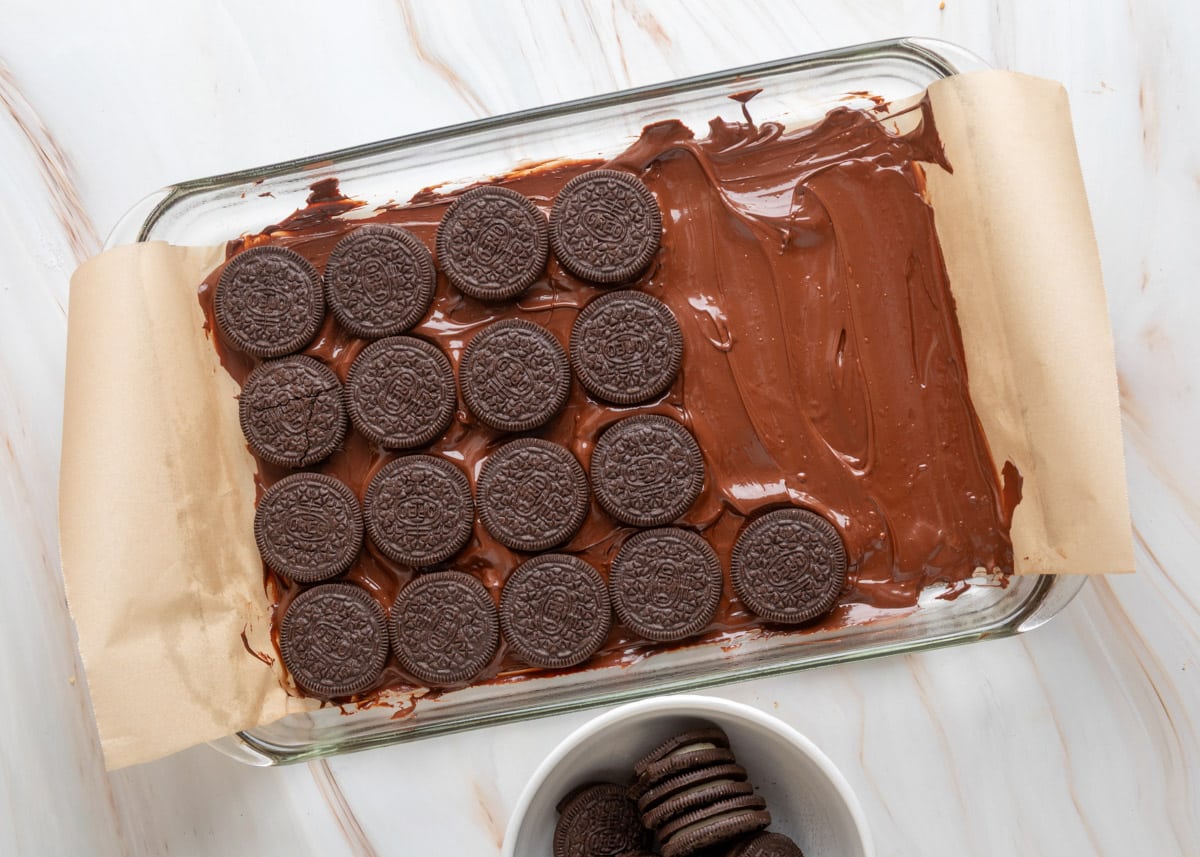 Step 2: Melt the Chocolate Base
In a microwave-safe bowl, melt the semi-sweet chocolate chips in short bursts, stirring between each. Start with 30 seconds on high. After that, switch to 15-second intervals until the chocolate begins to melt, then reduce to 10-second intervals so you don&rsquo;t overheat it.
Stir well after each round. Toward the end, the residual heat will often finish melting the smaller chips&mdash;give it a chance before microwaving again so the chocolate stays silky, smooth, and doesn&rsquo;t seize.
Spread the melted chocolate across the lined pan with your offset spatula to create an even layer. Then top the chocolate with a single layer of whole Oreo cookies (4 rows of 6 cookies).