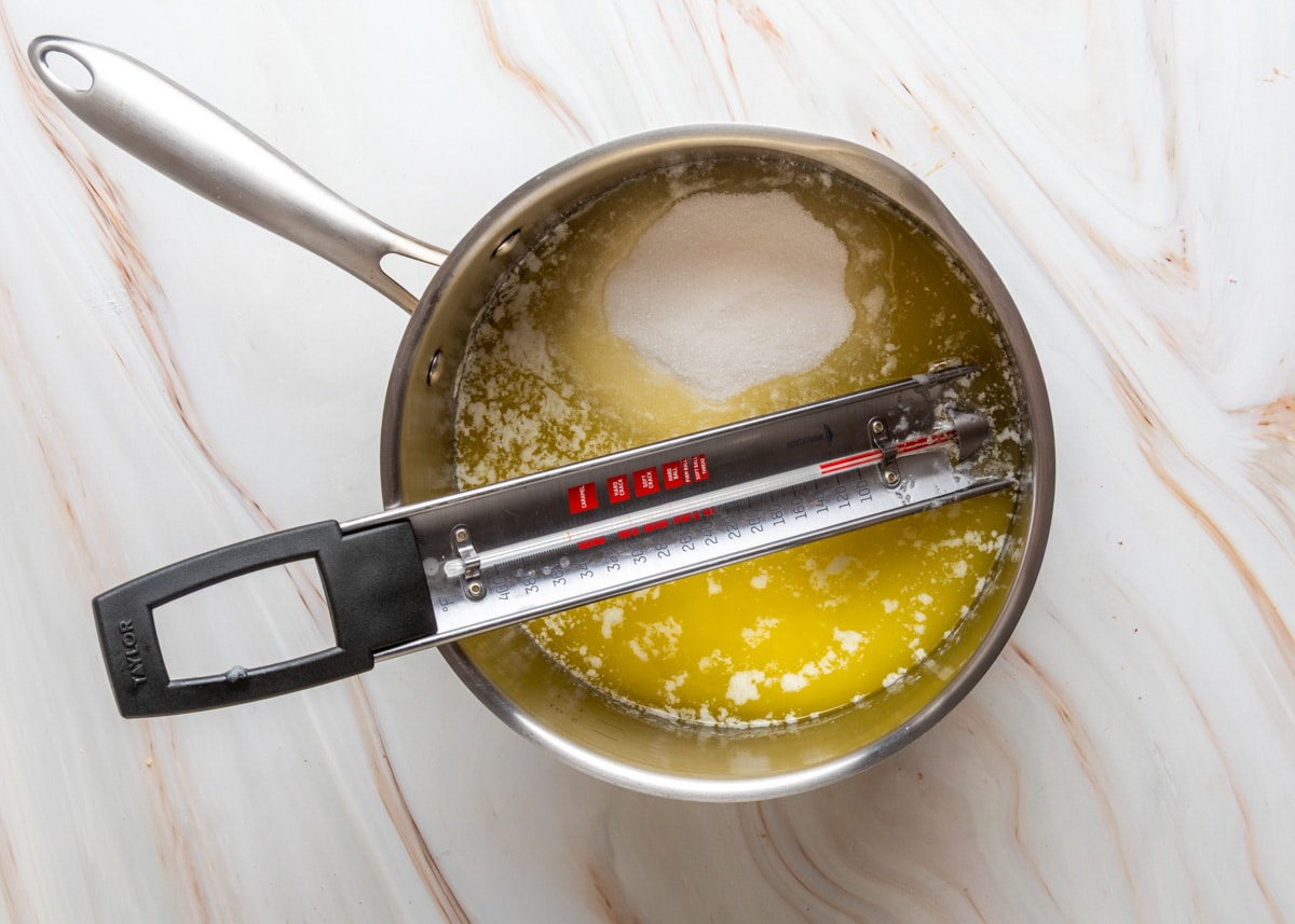 A saucepan of melted butter and sugar mixture at the beginning stages of toffee-making, with a candy thermometer clipped to the side.