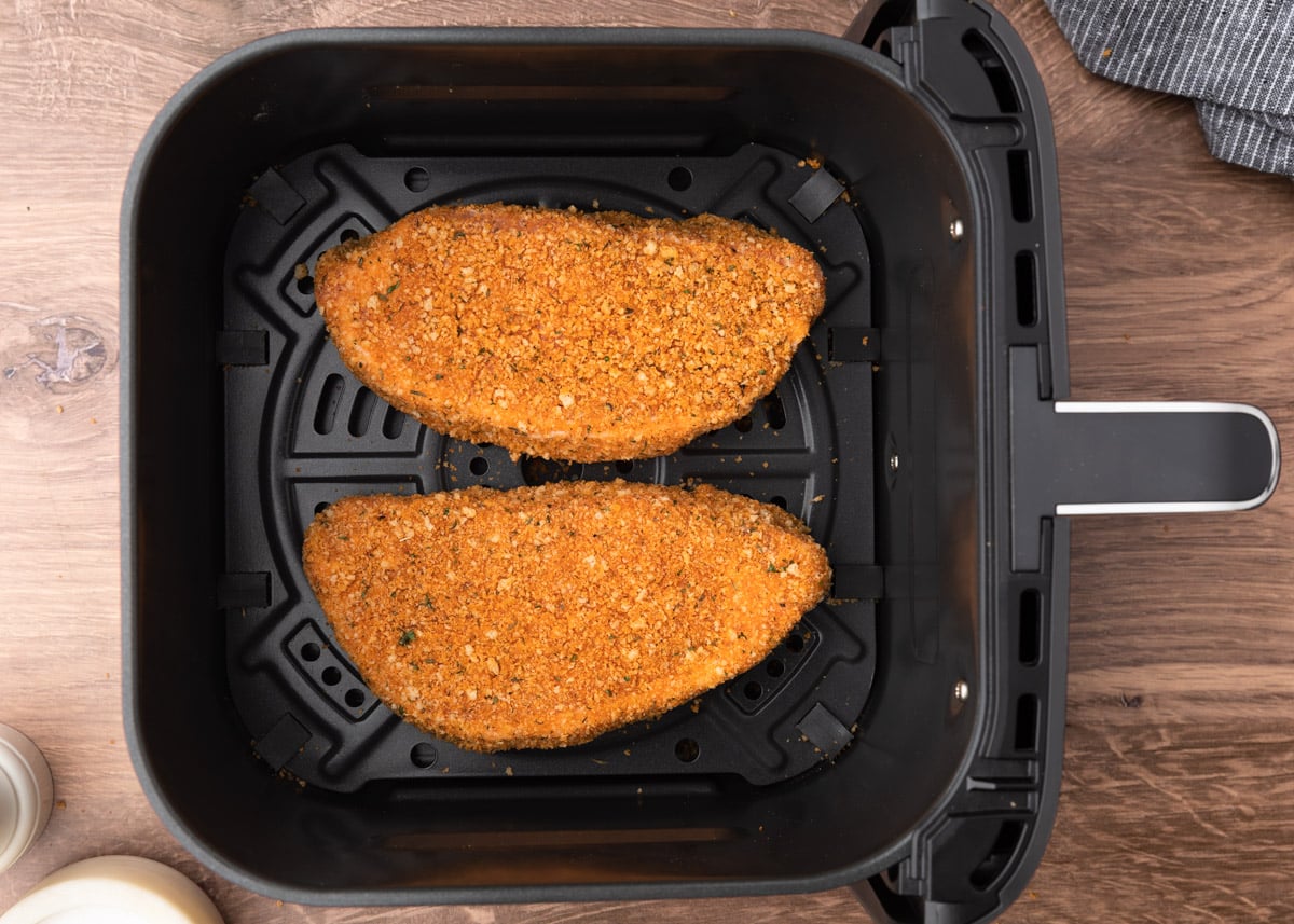 Two breaded pork chops placed side by side in the basket of an air fryer, ready to be cooked.
