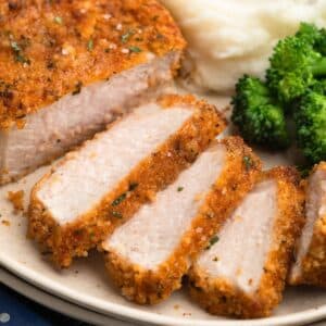 Sliced air fryer breaded pork chop with a crisp golden crust, served alongside mashed potatoes and steamed broccoli on a cream-colored plate.