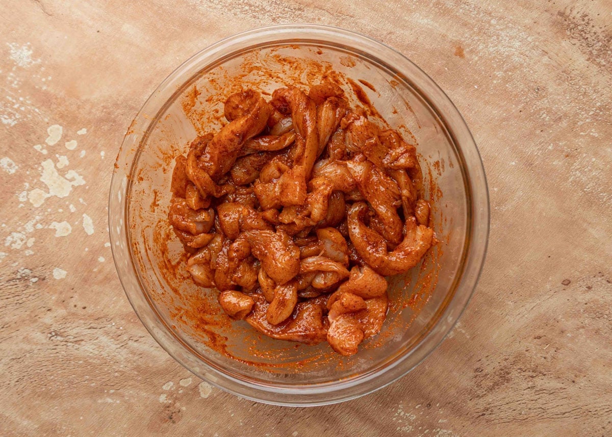 Raw chicken strips coated in a seasoned marinade in a glass mixing bowl, ready to be cooked for fajitas.