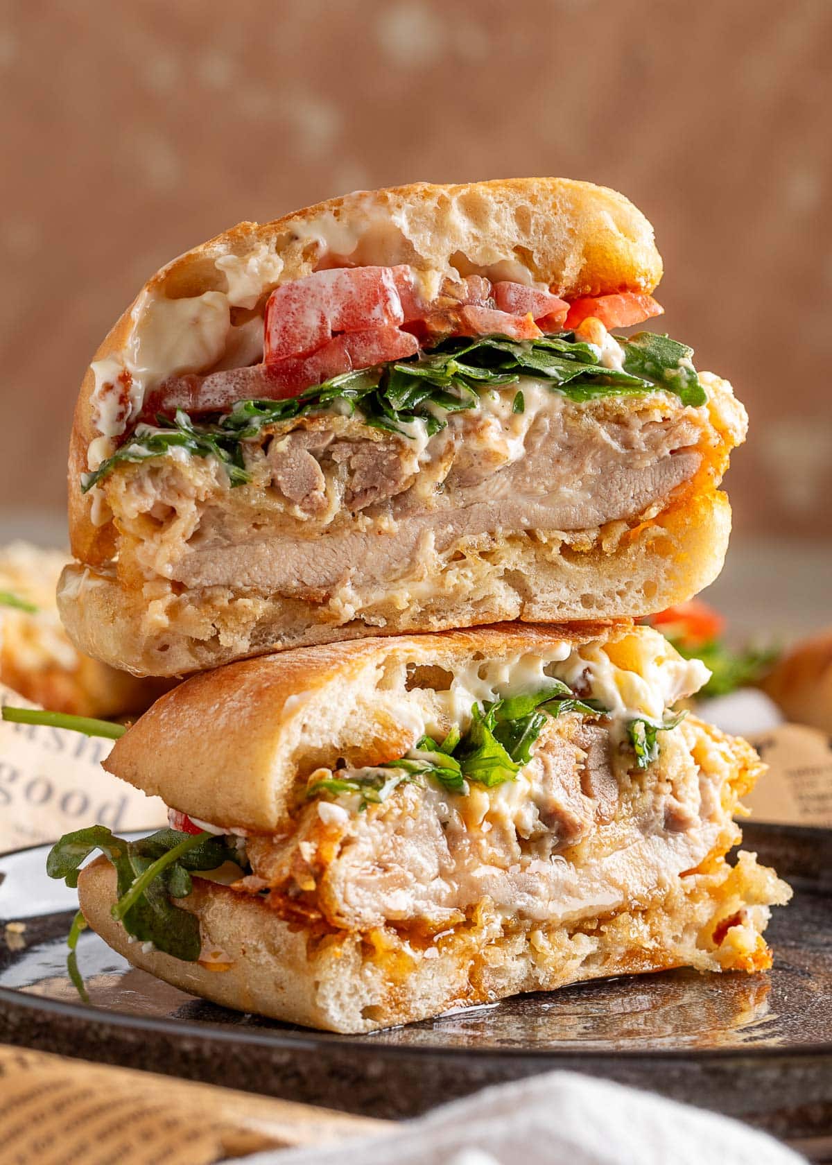 Stacked halves of a crispy chicken sandwich showing the juicy interior of the air-fried chicken thigh, fresh arugula, tomato, and creamy mayo on toasted sandwich rolls.