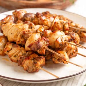 Close-up of juicy, golden-brown air-fried chicken souvlaki skewers stacked on a white plate, showing crispy edges and herb-seasoned pieces.