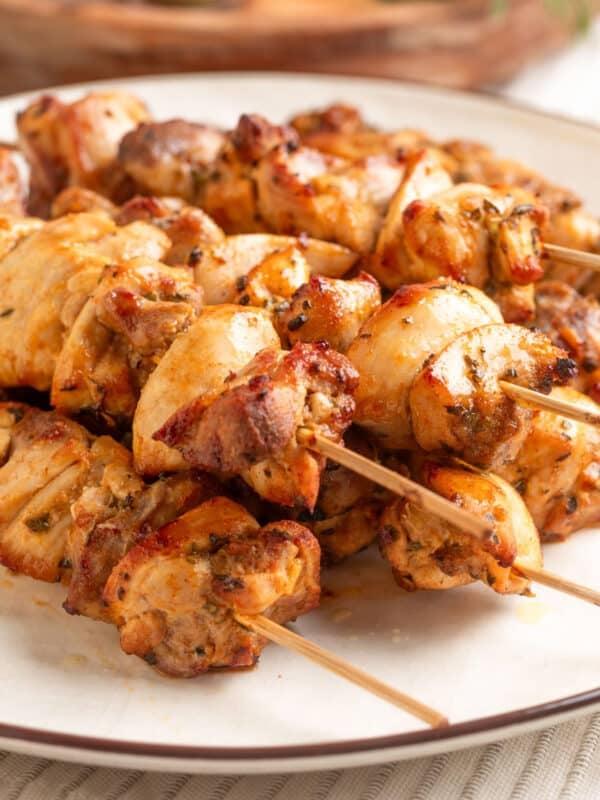 Close-up of juicy, golden-brown air-fried chicken souvlaki skewers stacked on a white plate, showing crispy edges and herb-seasoned pieces.