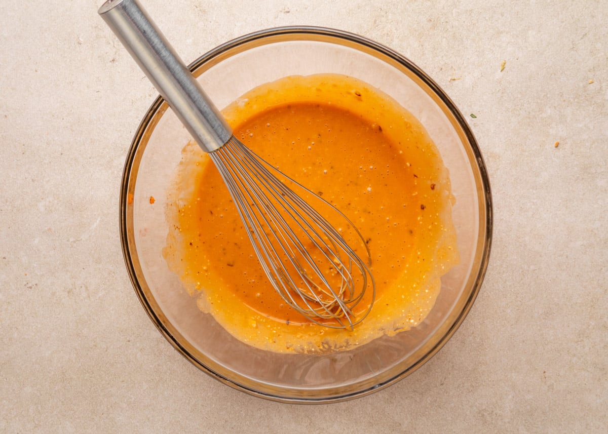 The finished bang bang dressing fully whisked in a glass bowl to a smooth orange consistency, with a metal whisk resting inside.