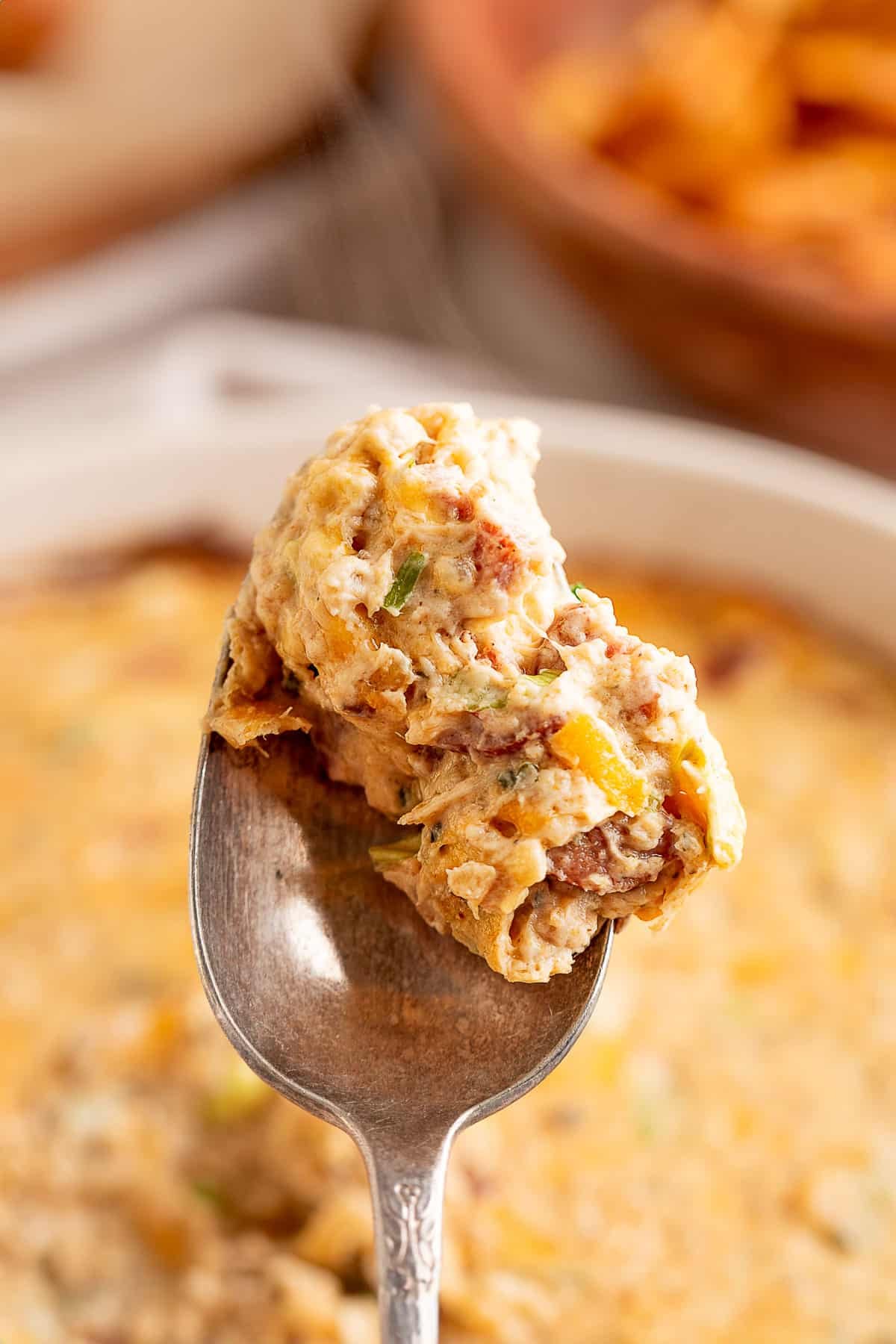 Close-up of a spoon lifting a steaming, creamy scoop of hot boudin dip showing bits of sausage, green onion, and melted cheese.