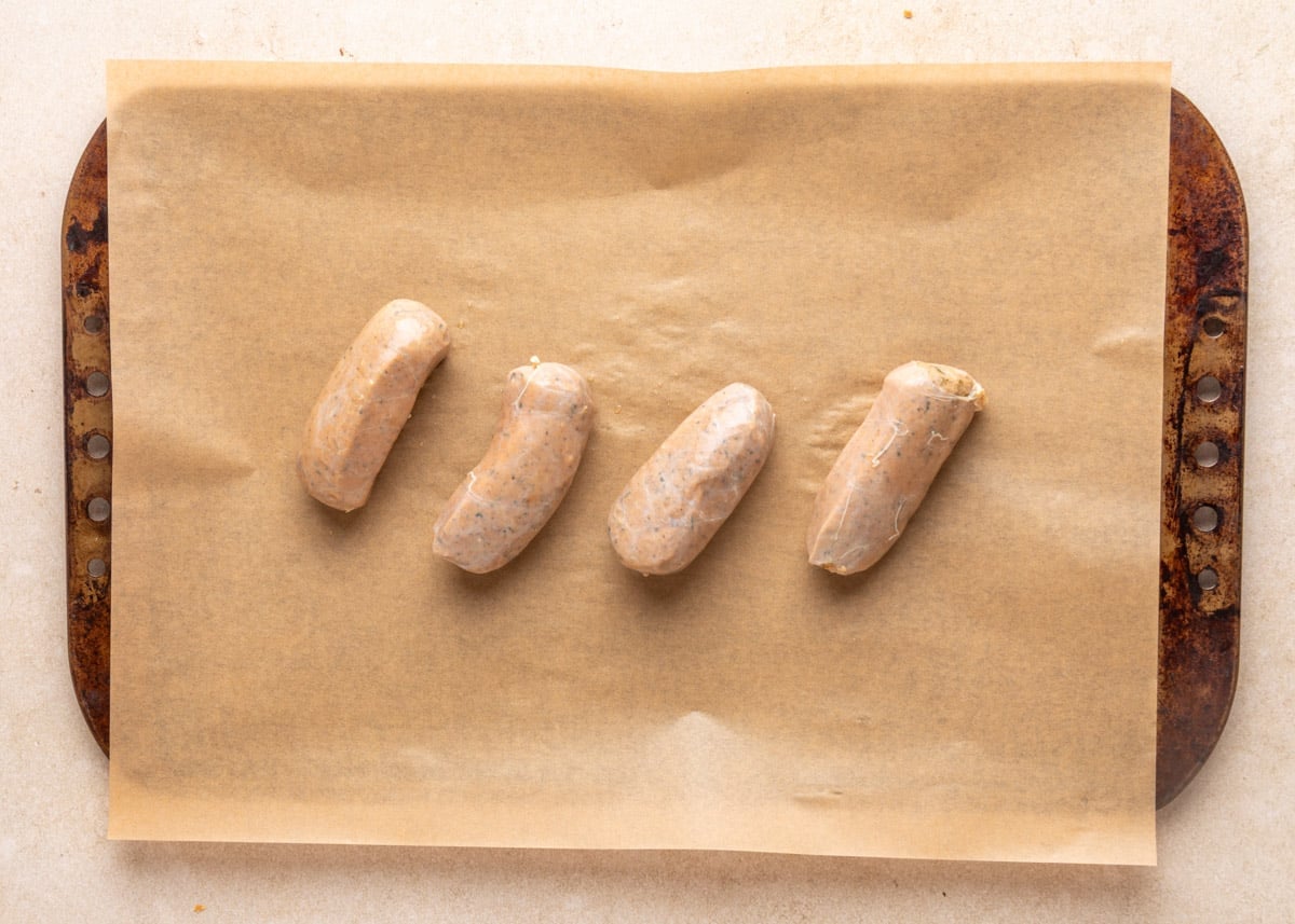 Four raw boudin sausage links arranged diagonally on a parchment-lined sheet pan before cooking.