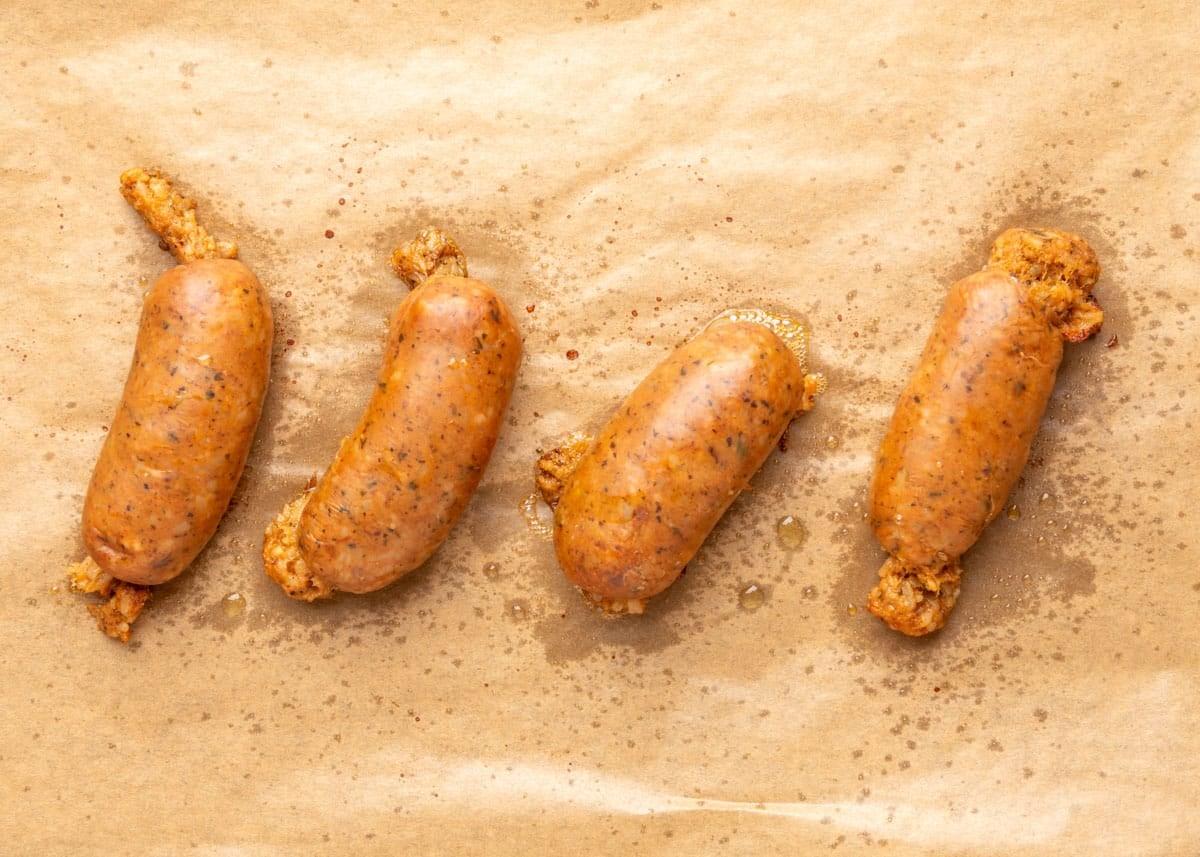 Four browned boudin sausage links arranged in a row on a parchment-lined baking sheet, glistening with rendered fat and lightly crisped at the edges.
