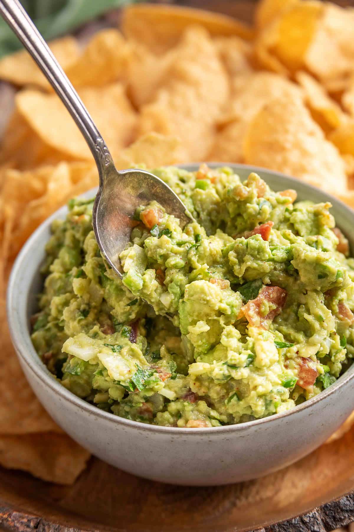 A close-up of a bowl of chunky guacamole with a spoon scooping out a portion, set against a background of golden tortilla chips.