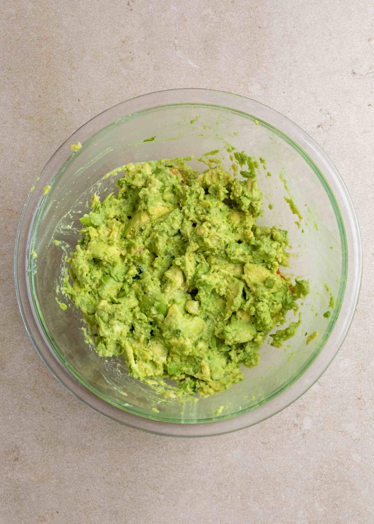 Partially mashed avocado in a glass bowl, showing a chunky guacamole base with visible avocado pieces.
