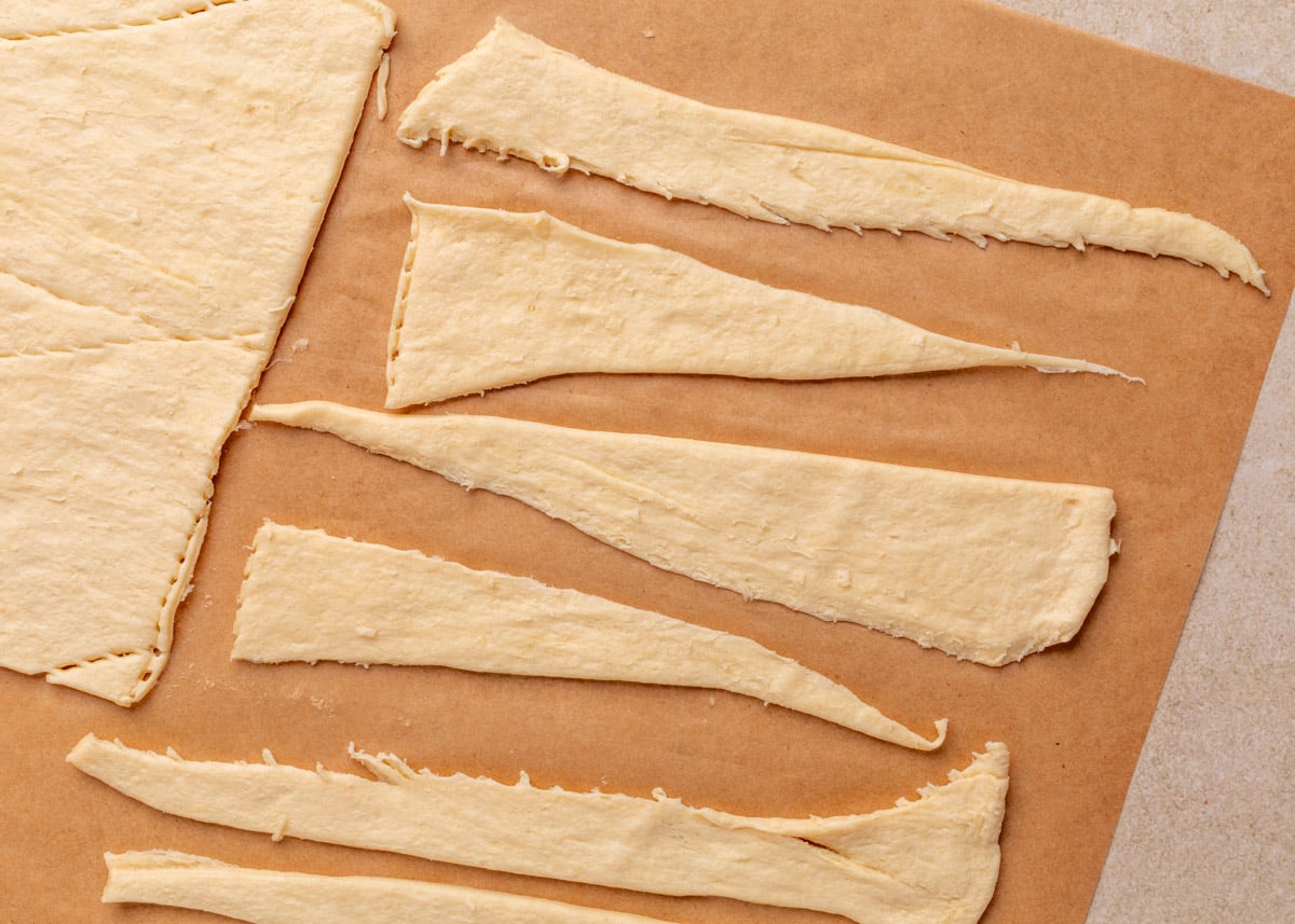 Unrolled crescent dough triangles arranged on a sheet of parchment paper, ready to be filled and rolled for Jalape&ntilde;o Popper Pigs in a Blanket.