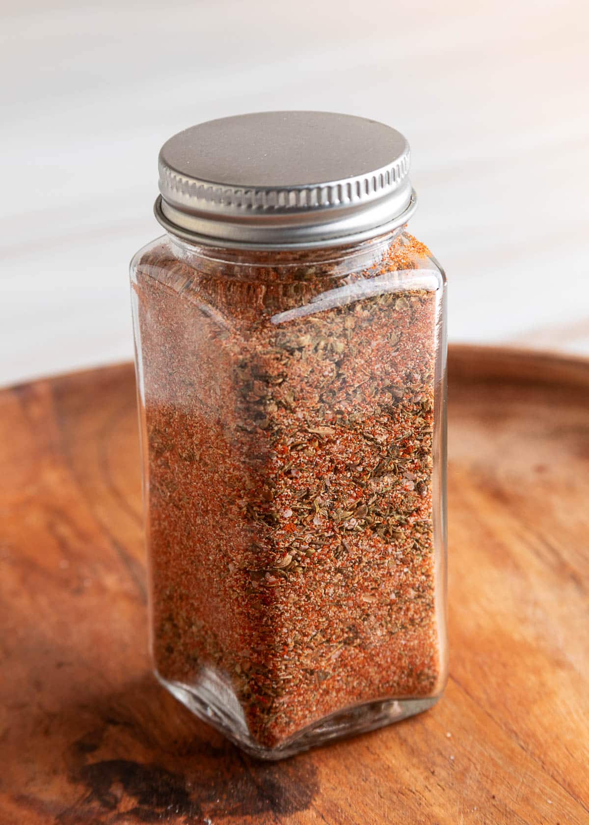 Homemade Creole seasoning packed into a square glass spice jar with a metal lid, set on a wooden surface.