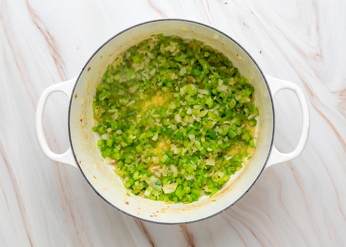 Overhead view of a Dutch oven with saut&eacute;ed diced onions, celery, and green bell peppers&mdash;known as the Cajun holy trinity&mdash;cooked in oil until softened.