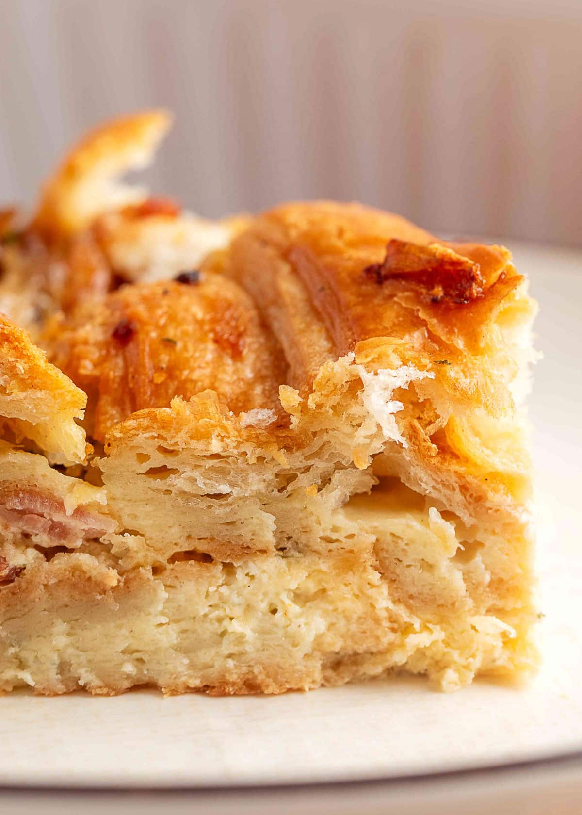 Close-up of a slice of sausage croissant breakfast casserole showing soft, custardy layers with croissants, sausage, and melted cheese.