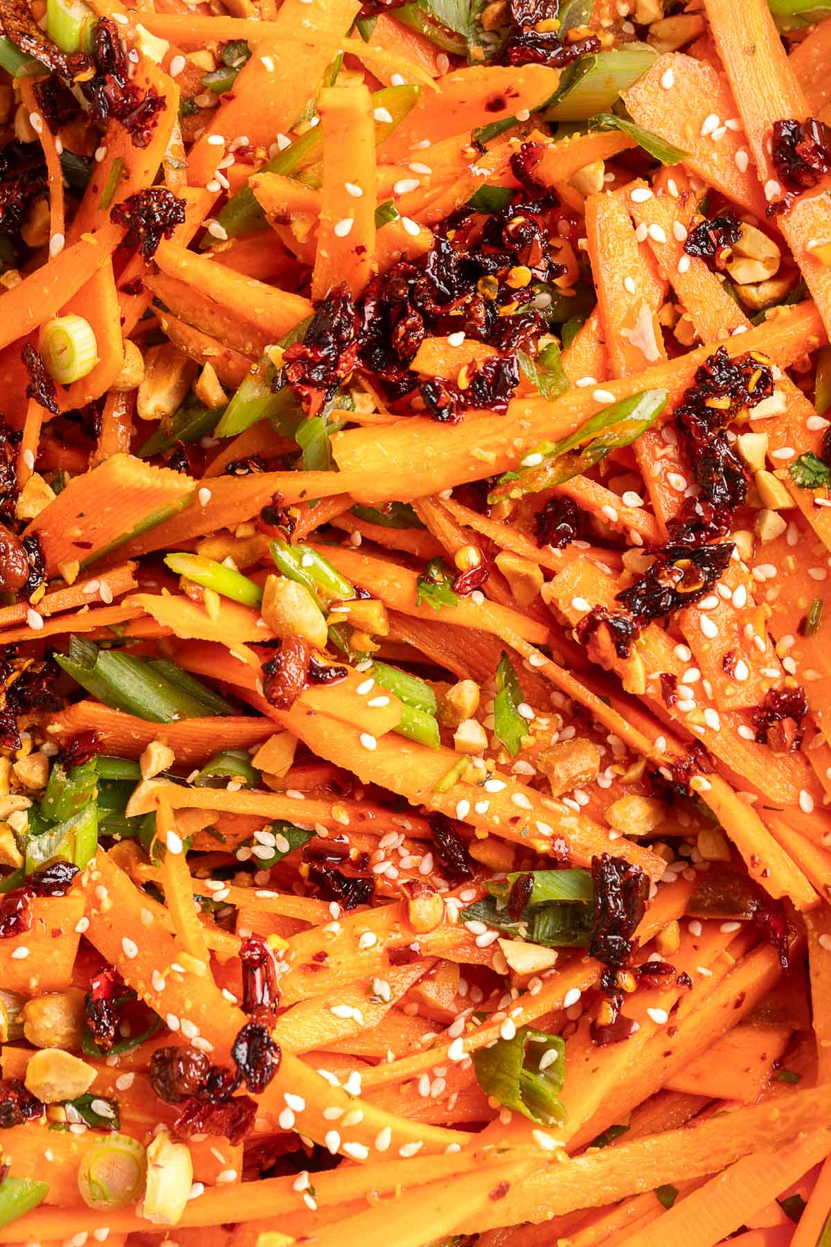 Close-up of carrot salad with shaved carrots, chili crisp, chopped peanuts, scallions, and sesame seeds tossed in a spicy sesame dressing.