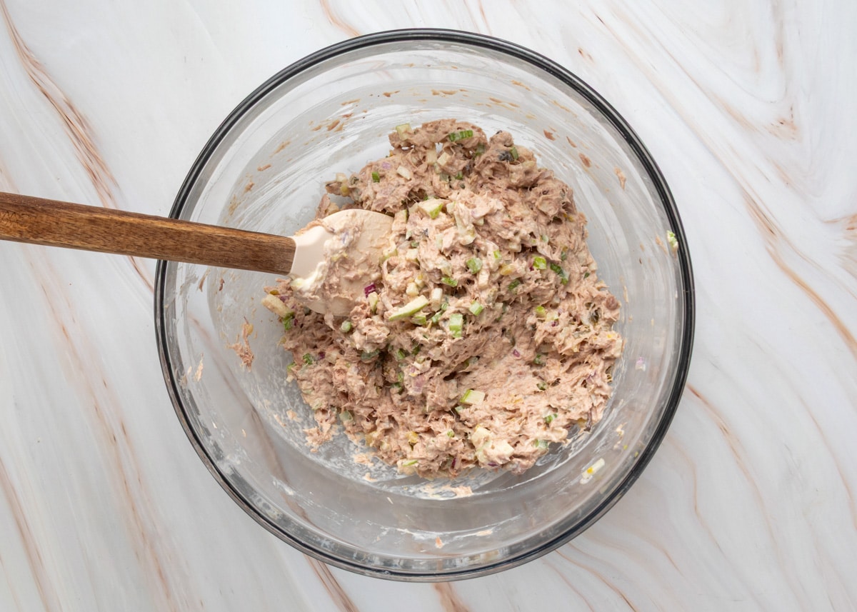 Apple tuna salad fully mixed in a glass bowl with visible chunks of apple, celery, and red onion.
