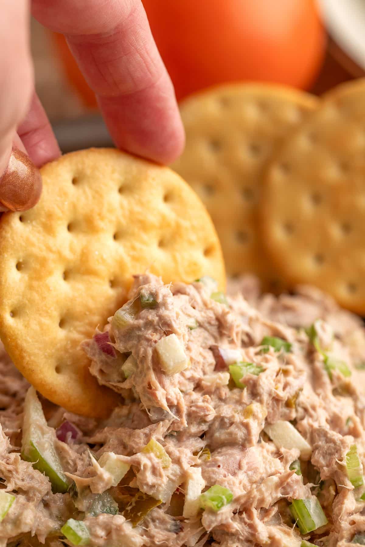 Butter cracker scooping apple tuna salad with visible chunks of celery, apple, and red onion.