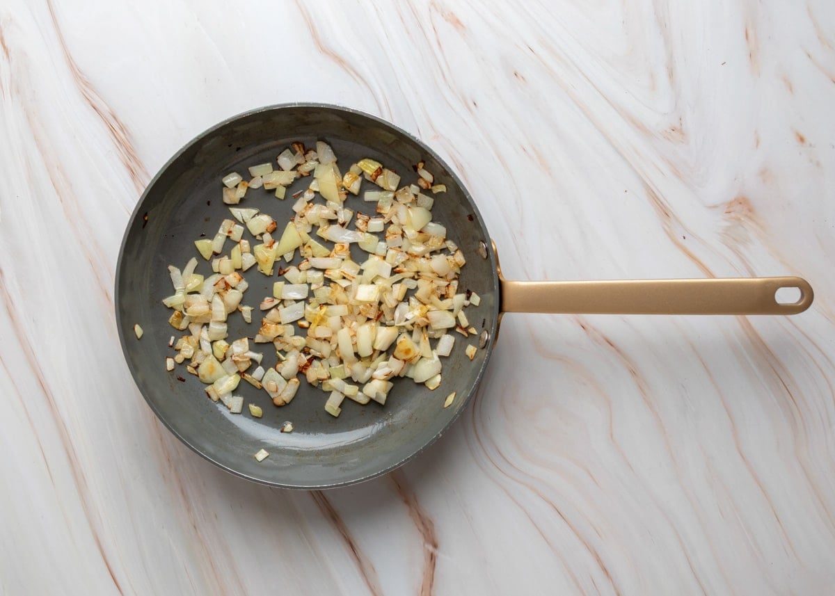 Overhead view of diced onions saut&eacute;ing in a skillet until softened and lightly browned.