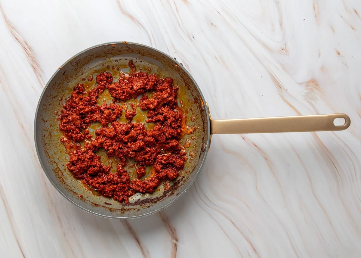 Overhead view of fresh pork chorizo cooking in a skillet, browned and crumbled with rendered orange-red oil in the pan.