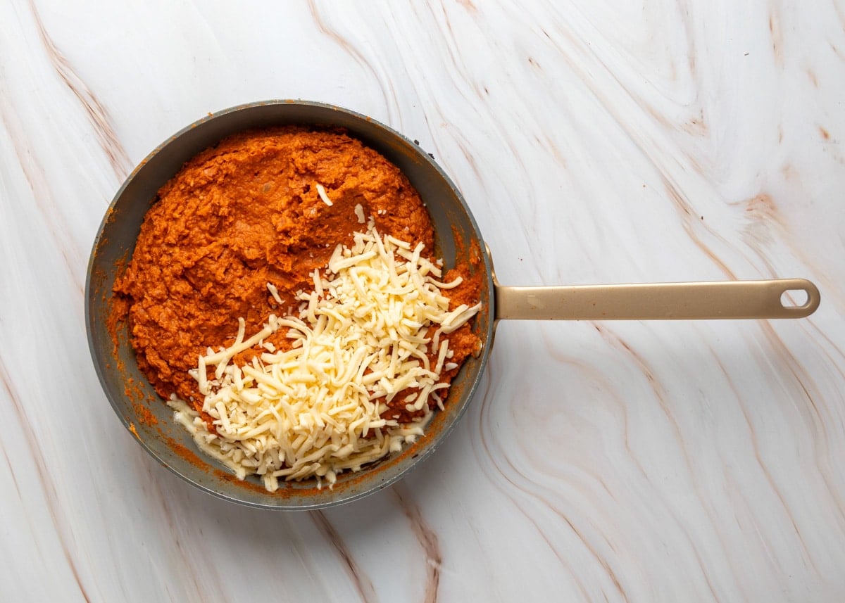 Overhead view of blended chorizo bean mixture in a skillet with shredded cheese added on top, ready to melt.