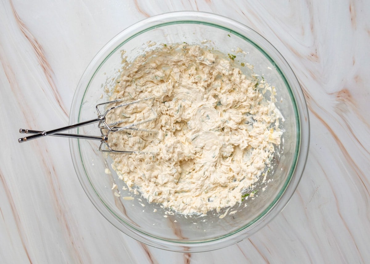 Crab rangoon dip mixture fully blended in a glass bowl with hand mixer beaters resting inside.