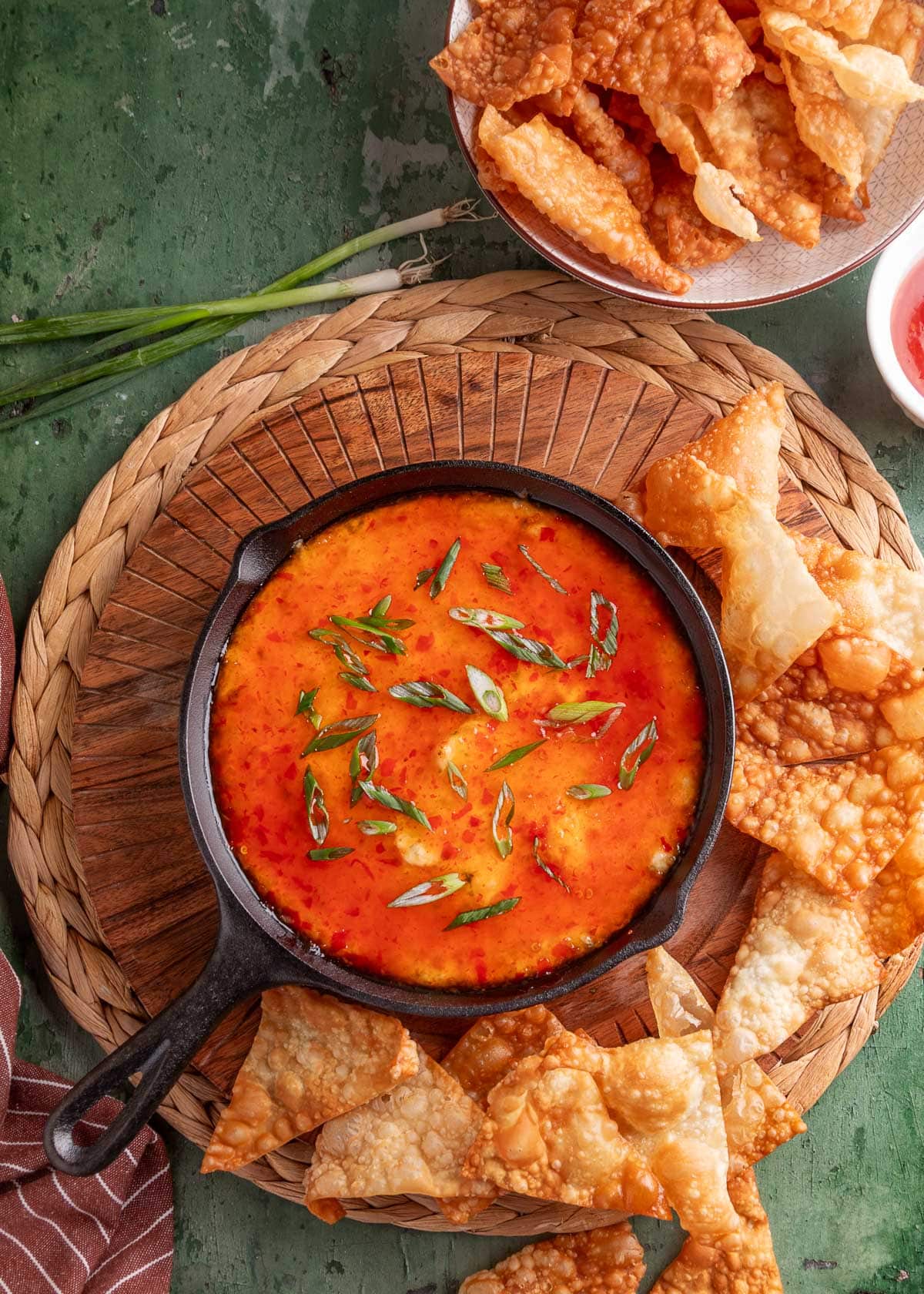 Crab rangoon dip baked in a skillet, topped with sweet chili sauce and scallions, served with crispy wonton chips for dipping.