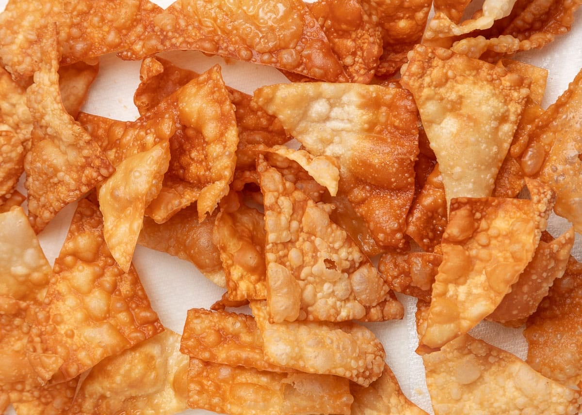 Close-up of crispy fried wonton chips, golden brown and blistered, piled together on a paper-lined surface.