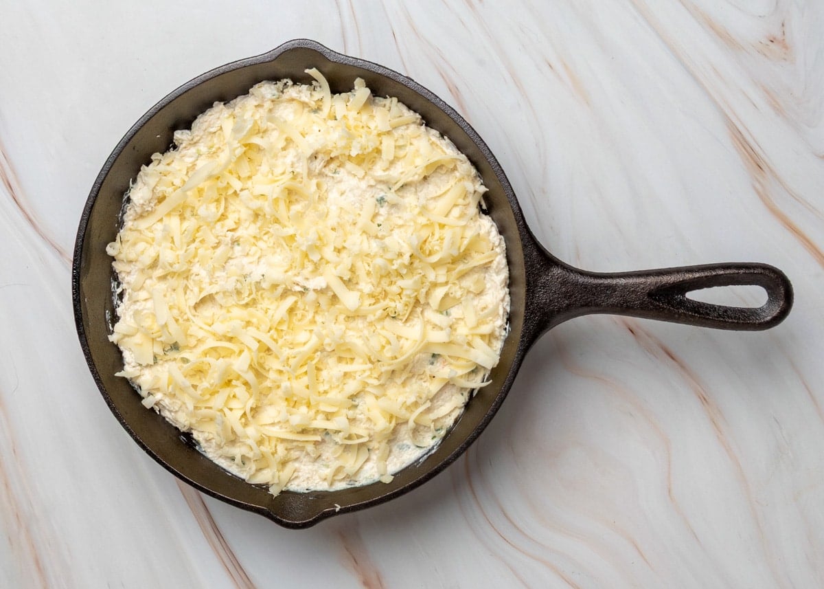 Overhead view of crab rangoon dip in a cast iron skillet, topped with shredded cheese before baking.