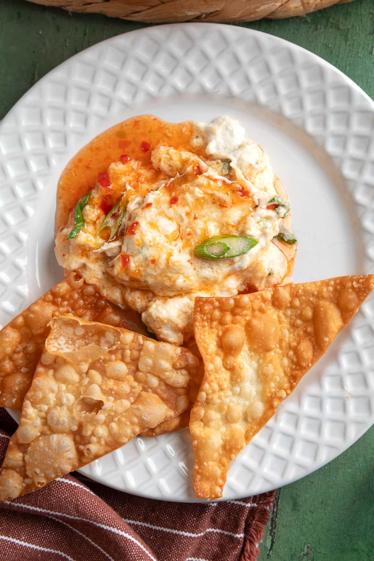 Crab rangoon dip drizzled with sweet chili sauce and topped with sliced green onions, served on a white plate with crispy wonton chips.