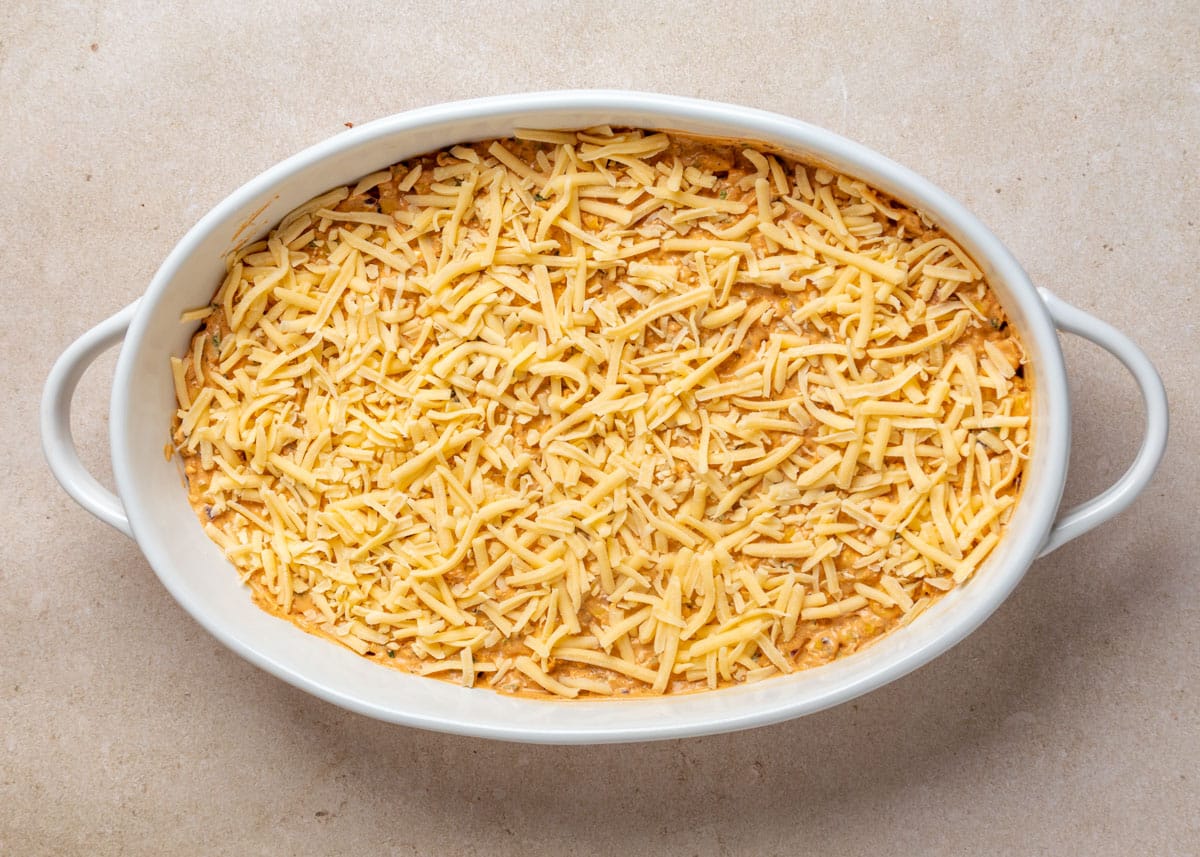 Overhead view of a baking dish filled with Mexican street corn dip, topped evenly with a layer of shredded cheese before baking.