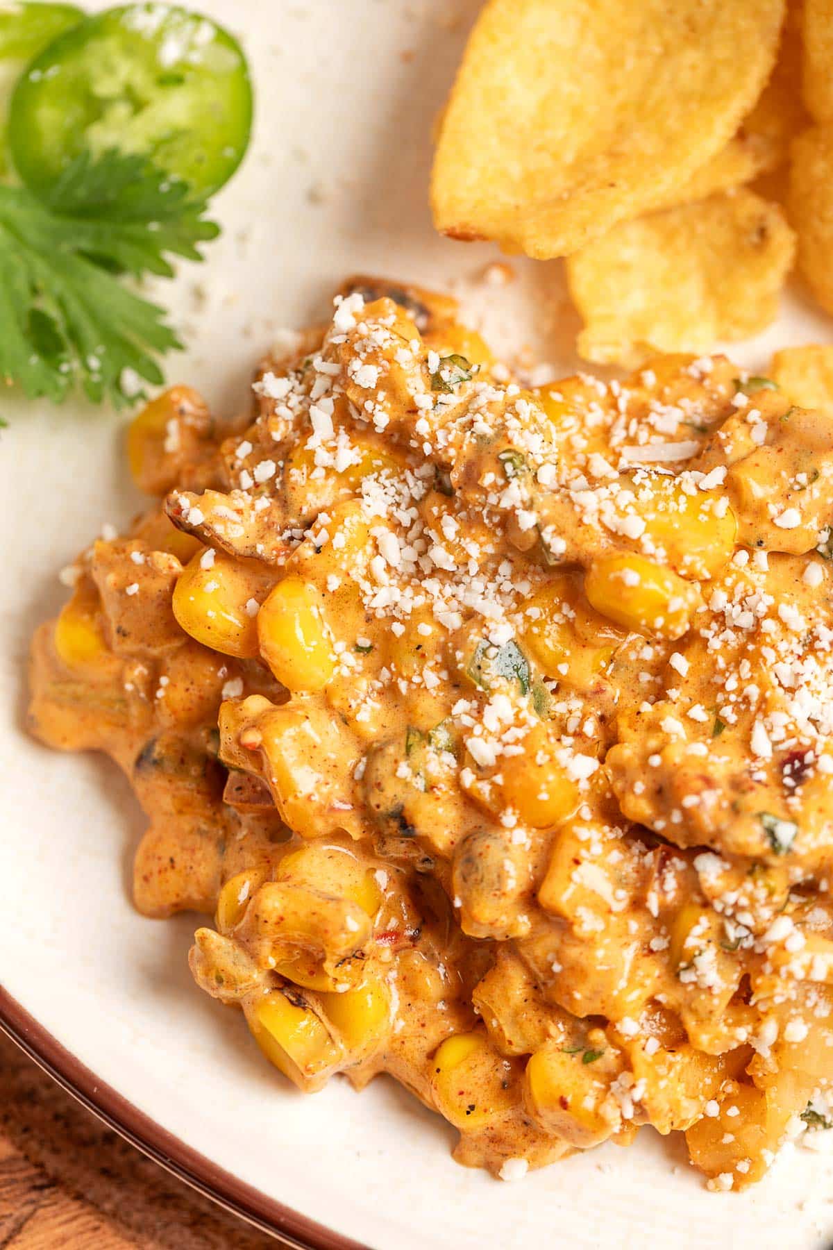 Close-up of a portion of Mexican street corn dip on a plate, showing creamy corn coated in a spiced sauce and sprinkled with crumbled cheese, with tortilla chips alongside.