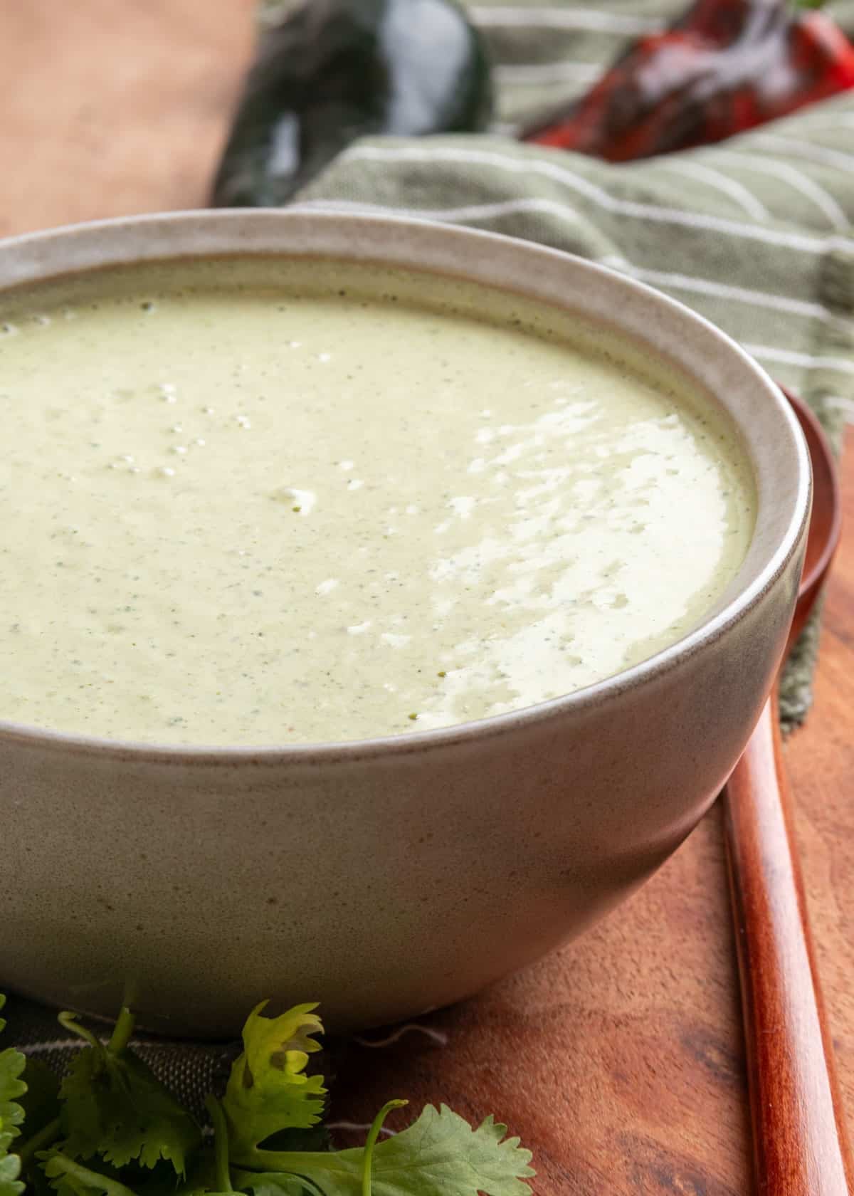 Close-up of creamy cilantro jalapeno dressing in a stoneware bowl on a wooden board, with fresh cilantro and a striped green kitchen towel in the background.