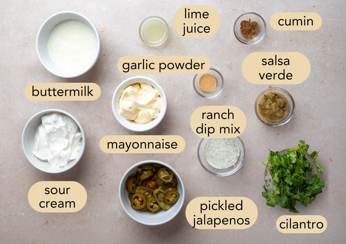 Overhead view of ingredients for creamy cilantro jalapeno dressing, including buttermilk, sour cream, mayonnaise, ranch dip mix, salsa verde, pickled jalapenos, cilantro, lime juice, cumin, and garlic powder.
